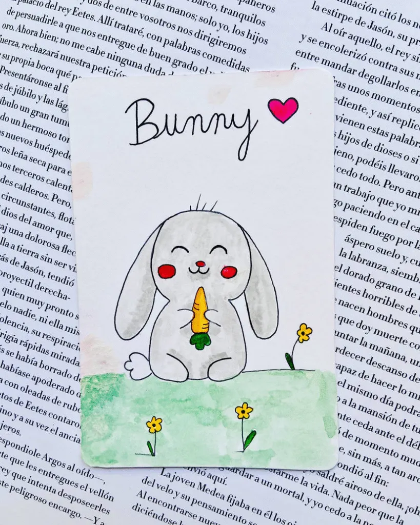 Hand-drawn bunny holding a carrot, with red cheeks and floppy ears, sitting on grass with little flowers.